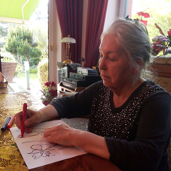 Annas Großmutter sitzt am Tisch und malt ein Bild aus.