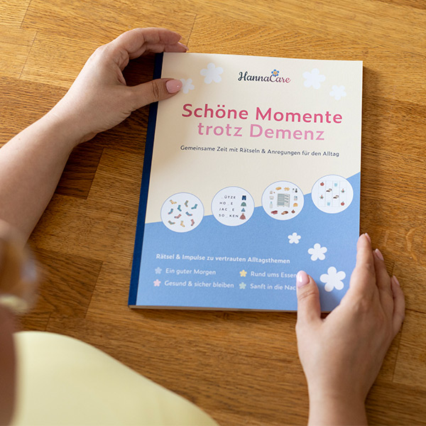 Beschäftigungsheft Schöne Momente trotz Demenz in den Händen gehalten Frau hält das Beschäftigungsheft Schöne Momente trotz Demenz in den Händen auf einem Holztisch