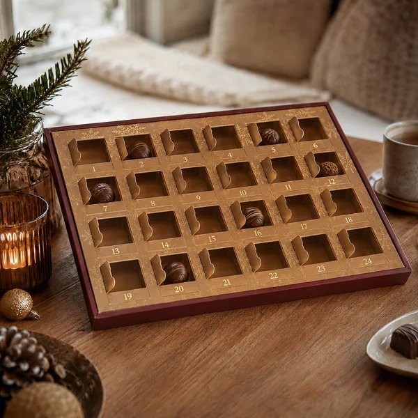 Geöffneter Pralinen-Adventskalender mit teilweise leeren Türchen und verteilten Pralinen auf einem Holztisch – Adventskalender als Geschenk bei Demenz schwierig