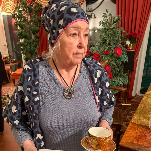 Hannelore trägt eine gemusterte Mütze und hält eine Kaffeetasse – Schal und Mütze als Geschenk an einem Weihnachtsabend bei Demenz