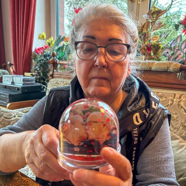 Hannelore hält eine Schneekugel mit einem Foto in den Händen und betrachtet sie irritiert – nicht jedes personalisierte Geschenk wird bei Demenz verstanden