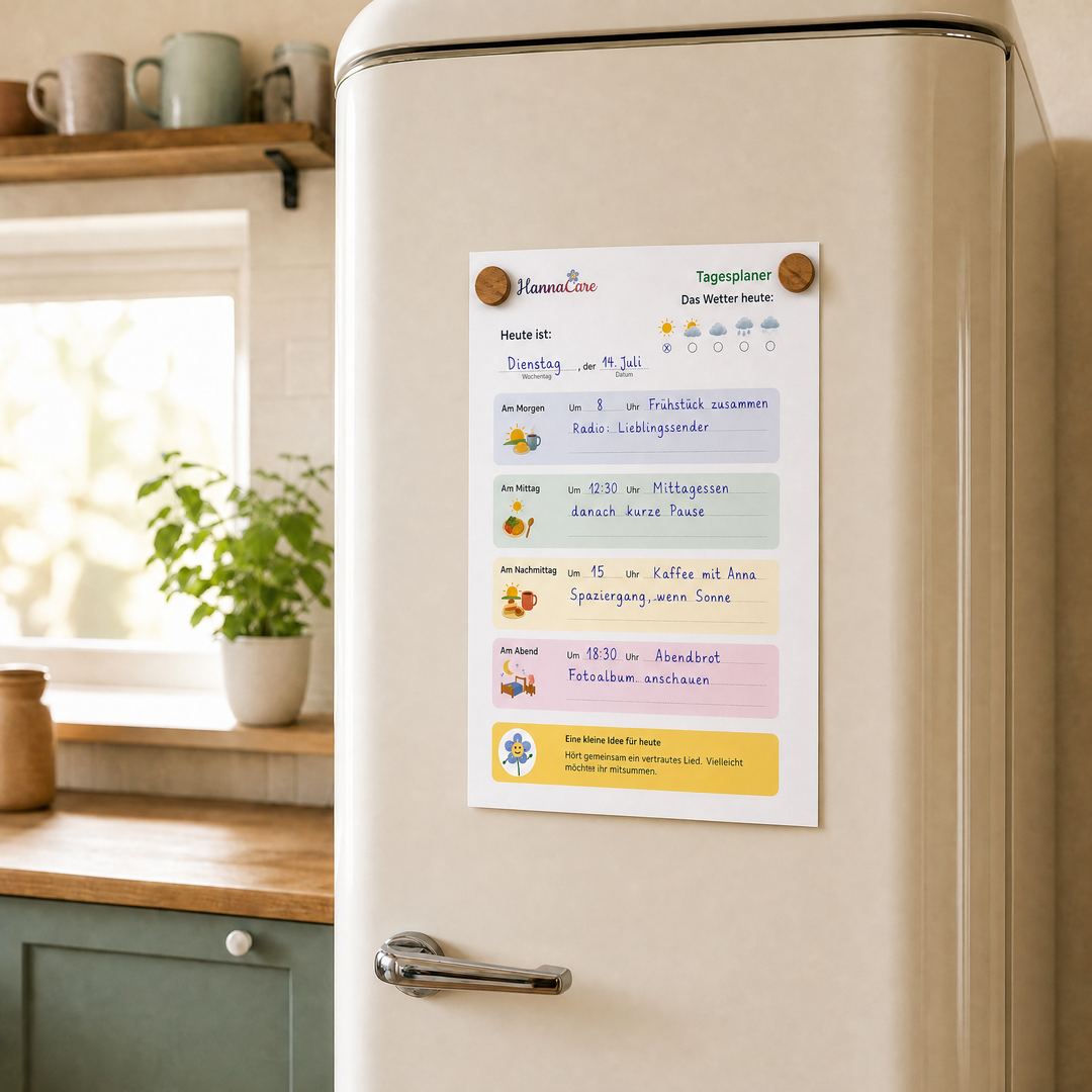 Ausgefüllter HannaCare Tagesplaner bei Demenz hängt mit zwei Holzmagneten am Kühlschrank in einer hellen Küche – A4-Tagesblatt mit Wochentag, Wetter, vier Tagesabschnitten und einer kleinen Idee für heute