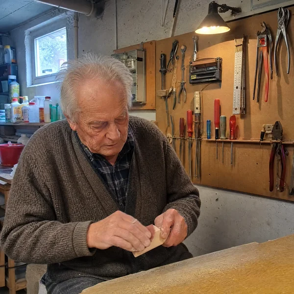 Aktivierung für Männer mit Demenz: Ein älterer Herr schleift in seiner Kellerwerkstatt ein Stück Holz mit Schleifpapier.