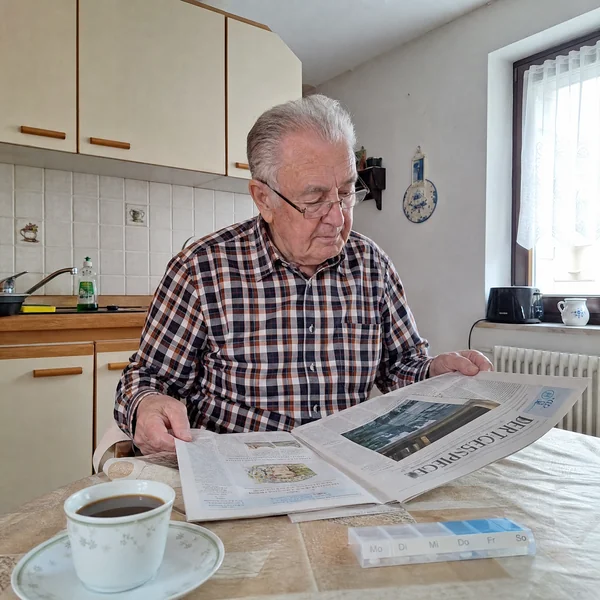 Beschäftigung bei Demenz zu Hause: Ein älterer Mann blättert am Küchentisch in der Tageszeitung, daneben eine Tasse Kaffee.