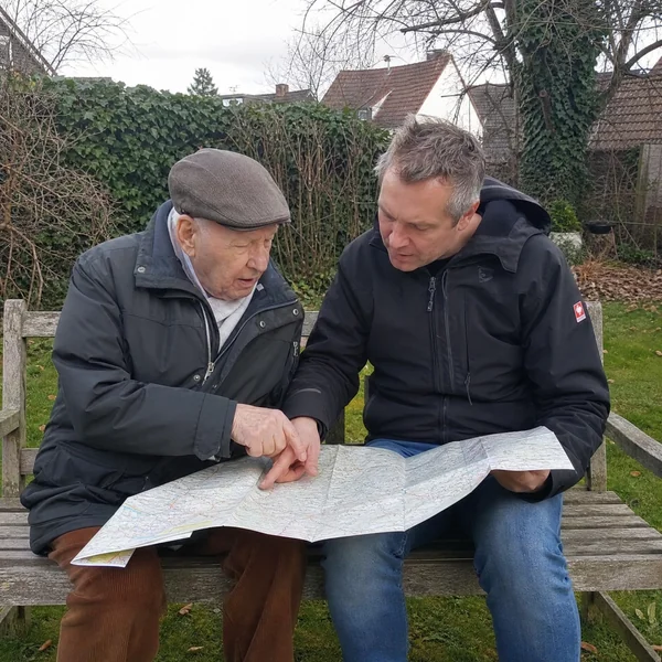 Biografiearbeit bei Demenz: Ein älterer Mann mit Schiebermütze und sein Sohn schauen gemeinsam auf einer Gartenbank eine alte Landkarte an.