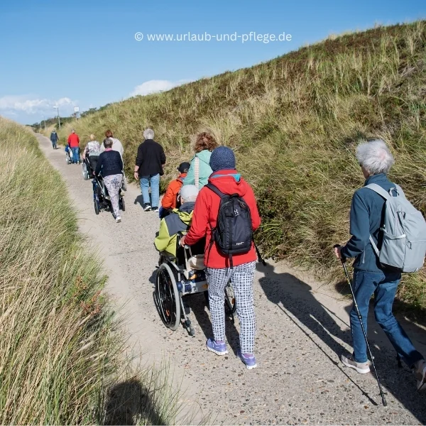 Reisen für Menschen mit Demenz: Reisegruppe mit Rollstuhl und Begleitern wandert auf einem barrierefreien Weg durch die Dünen